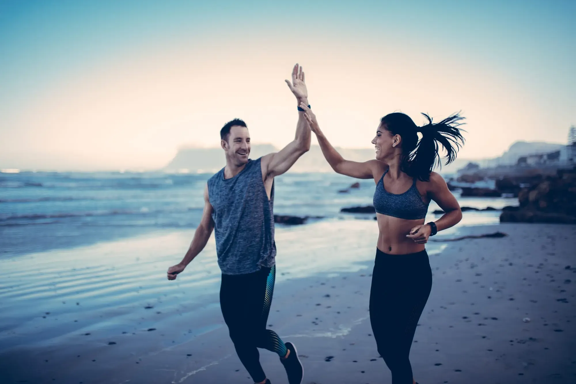 Fit couple high-fiving after a run on the beach at sunset